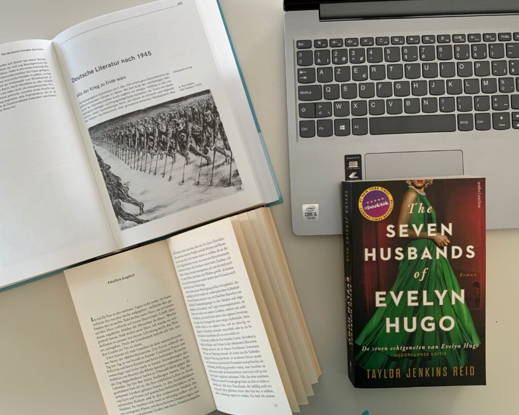 Laptop omringd door opengeslagen studieboeken en 'The seven husbands of Evelyn Hugo'